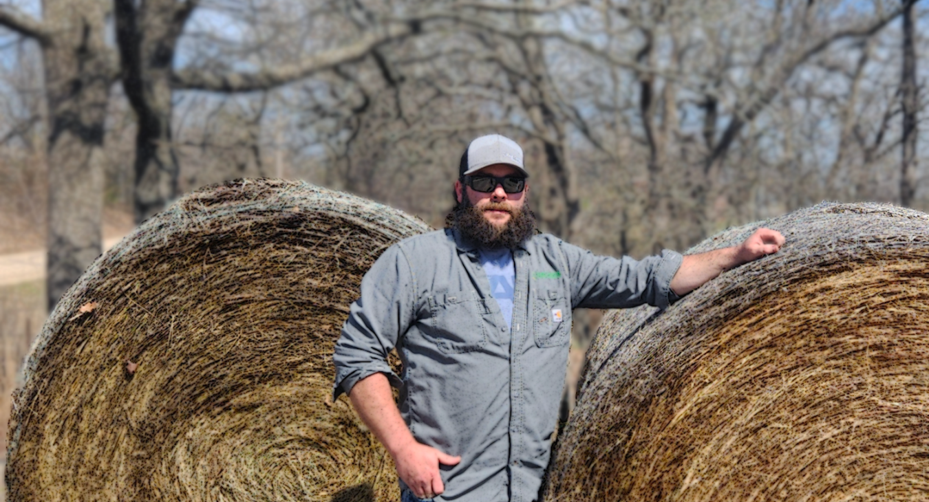 ECE Lineman Brad Duncan standing between round bales of hay